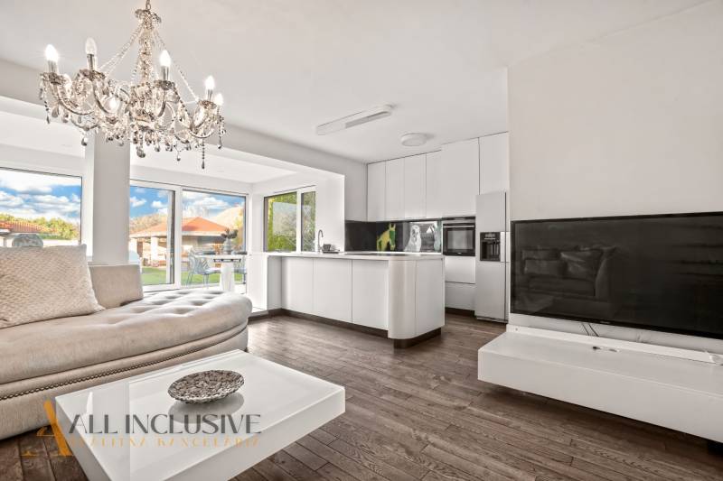 Living room and kitchen with a chandelier, sofa, white furniture, and wood-patterned flooring.