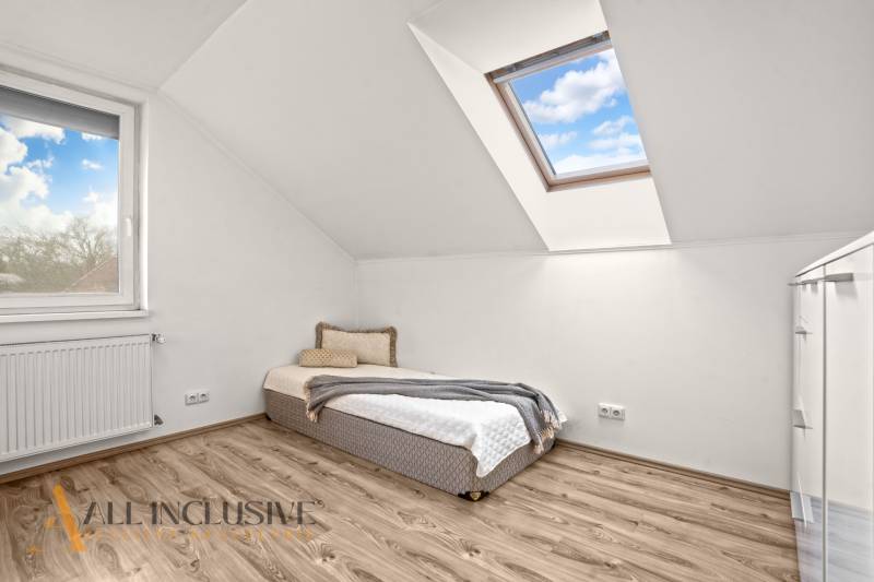 Attic room in a family house with a bed and a skylight, floor with wooden decor.