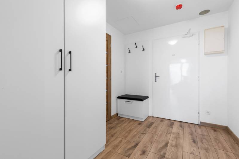 Entrance area with white cabinet furniture, a bench, and a wooden decor floor in a 3-room apartment.