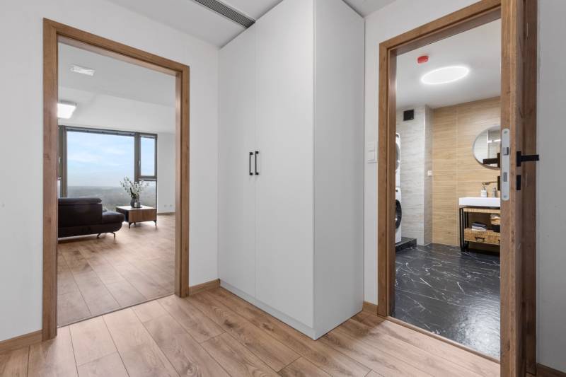 Interior of a 3-room apartment with a wooden decor floor, white cabinets, and a bathroom.