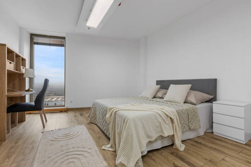 A bedroom in a 3-room apartment with a wood-decor floor, a bed, and a desk.