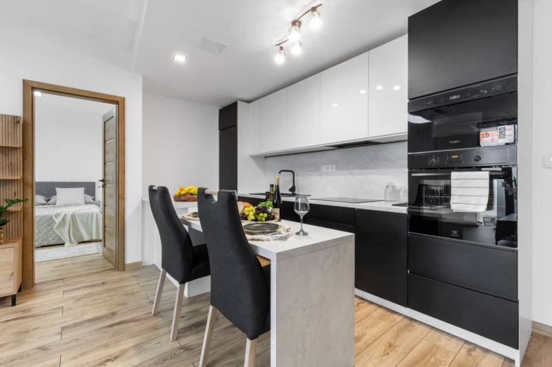 A kitchen in a 3-room apartment with dark cabinets, a dining table, and a wooden decor floor.