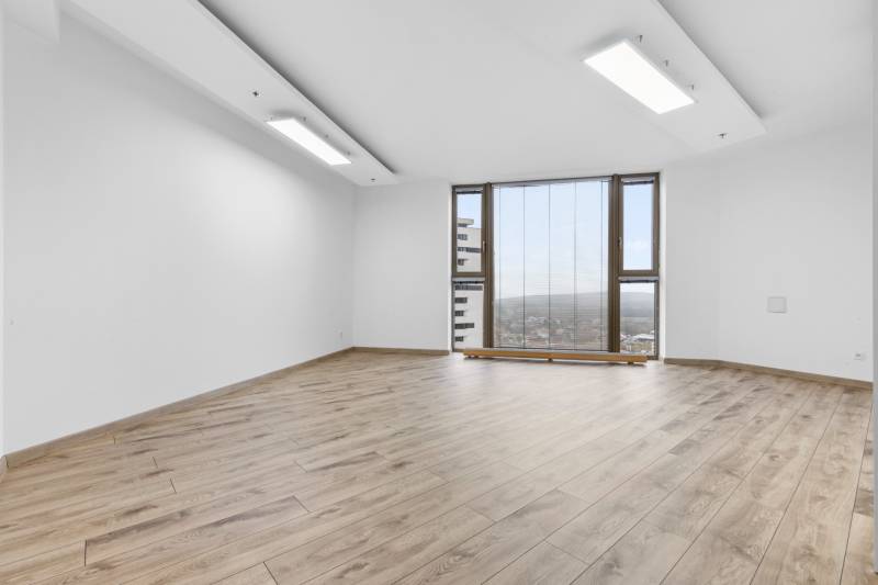 A bright room with a wood-patterned floor and large windows in a three-room apartment.