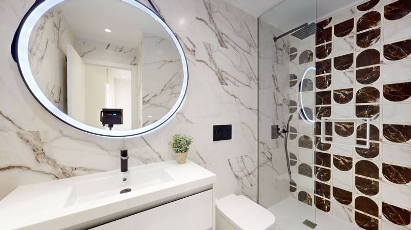 A bathroom in a holiday apartment with a round mirror and a shower corner.
