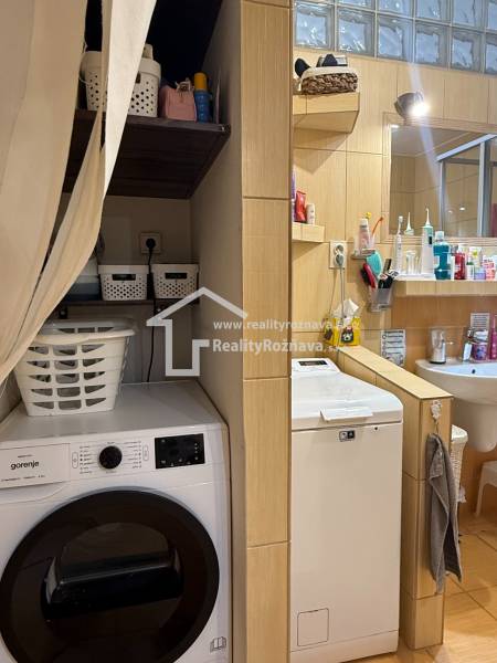 A bathroom in a 3-room apartment with a washing machine, shelves, and a sink, with a wooden decor floor.