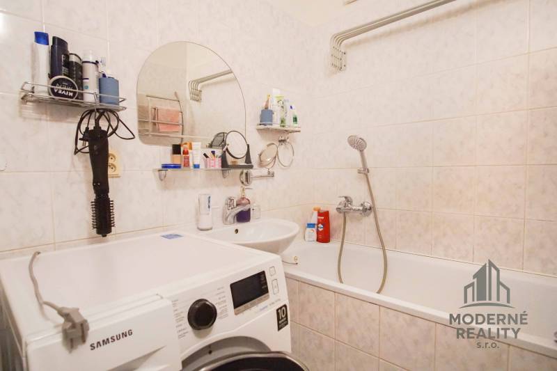 A bathroom in a 3-room apartment with a bathtub and a washing machine, accessories on the shelves.