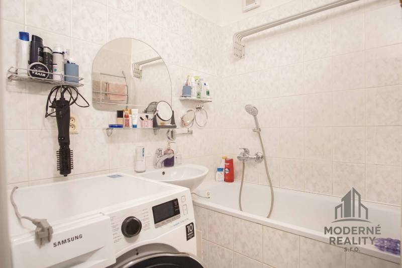 A bathroom of a three-room apartment with a washing machine, a sink, and a bathtub.