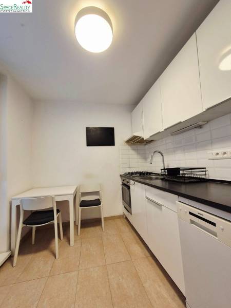 A kitchen in a 2-room apartment with white cabinets, a dining table, and appliances.