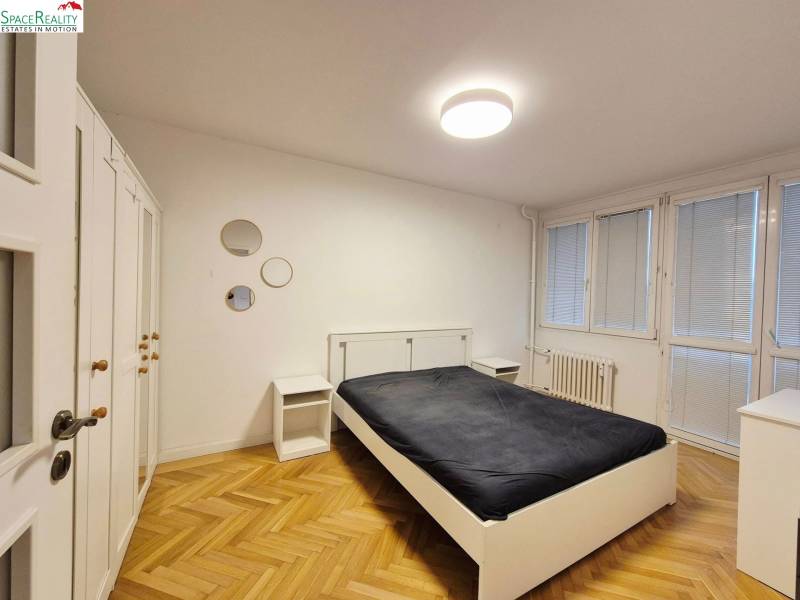 Bedroom in a two-room apartment with wood-patterned flooring and white furniture.