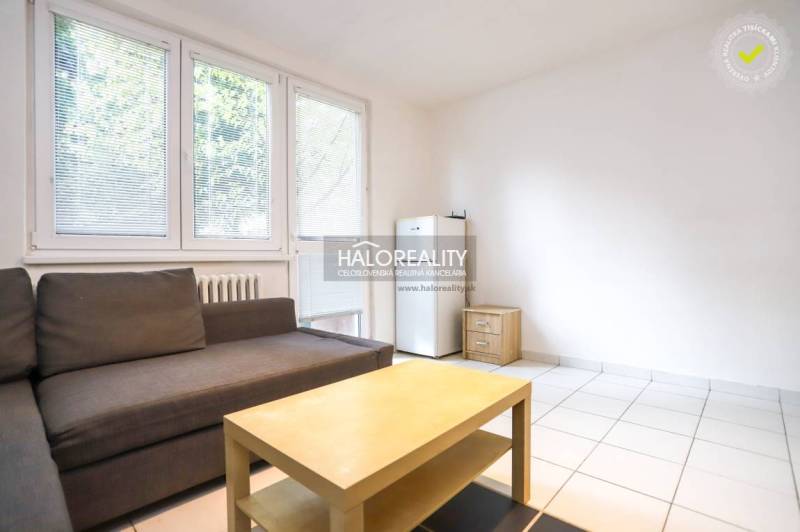 Living area of a studio apartment with a sofa, table, and refrigerator.