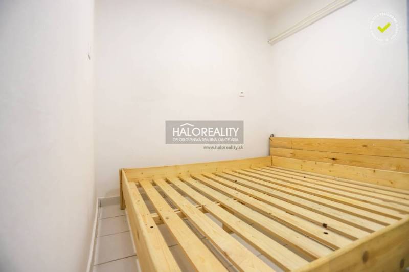 A bedroom in a one-room apartment with a wooden bed and white walls.