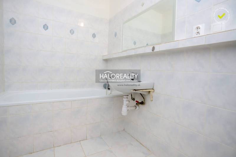 Bathroom in a one-room apartment with a bathtub, sink, and tiled cladding.