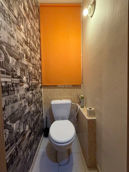 A toilet with graphic wallpaper and orange blinds in a 3-room apartment.