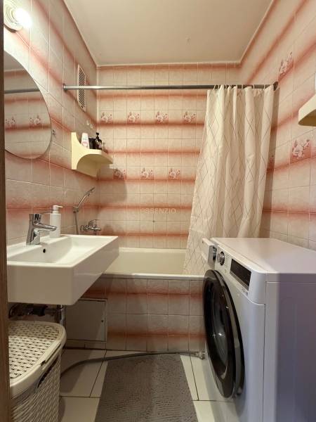 A bathroom with a washing machine, bathtub, and sink in a 3-room apartment, tiled with a pink pattern.