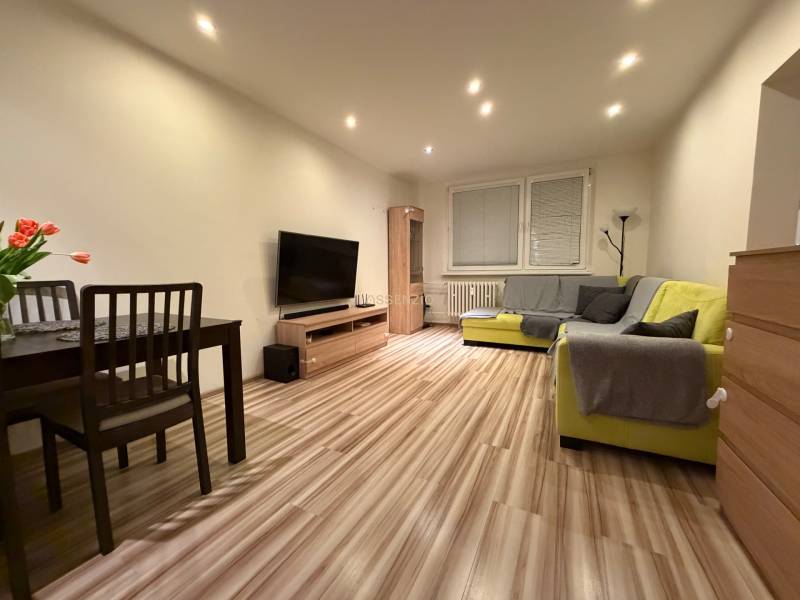 Living room with a sofa, dining table, and wood-patterned flooring in a 3-room apartment.