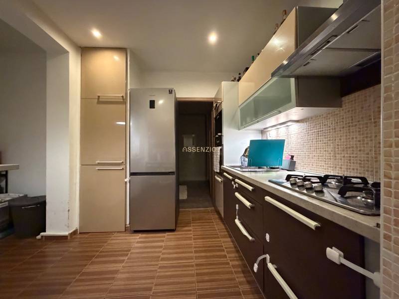 A kitchen in a 3-room apartment with a gas stove, refrigerator, and wooden decor flooring.
