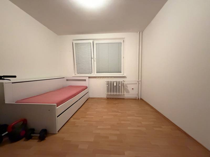 A room in a three-room apartment with a bed, blinds, and a floor with a wood decor.