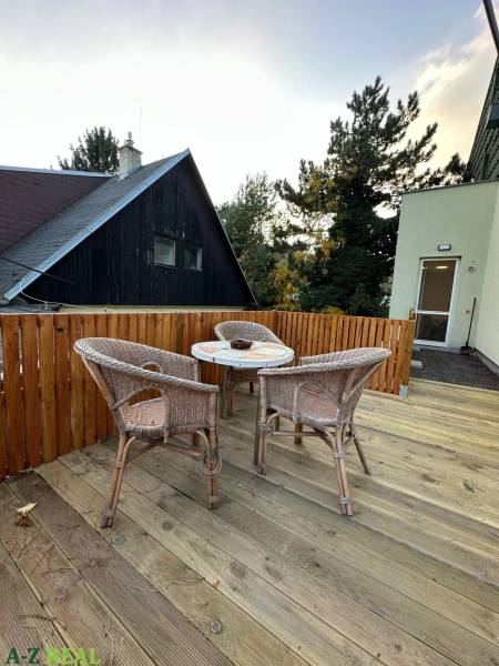 A terrace with rattan seating and wooden decor, surrounded by greenery.