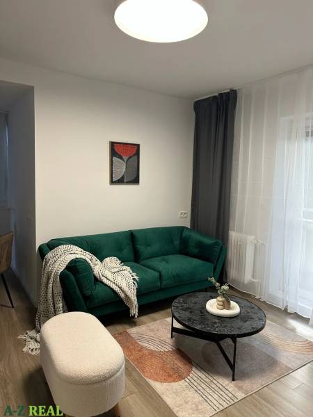 Living room in a three-room apartment with a dark green sofa, a round table, and a wooden decor floor.