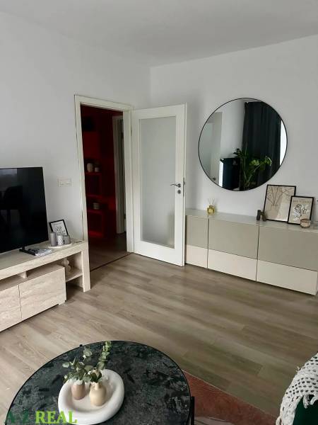 Living room in a three-room apartment with a wooden decor floor, a television, and a round mirror.