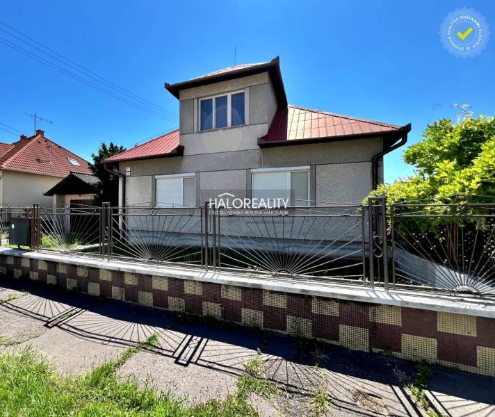 A family house in Levice with a metal fence and a sloped roof on a sunny plot.