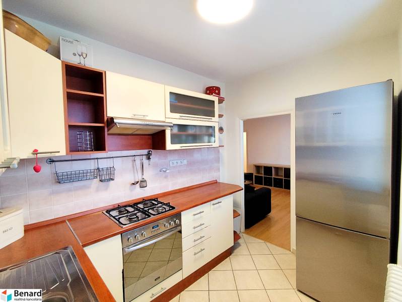 A kitchen in a 3-room apartment with a gas stove, stainless steel refrigerator, and wooden decor flooring.
