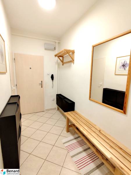 A hallway in a 3-room apartment with tiles, a wooden bench, and a mirror on the wall.