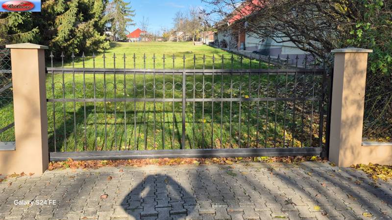 A metal gate surrounded by pillars and greenery in Veľké Ludince on Park Street and the main road.