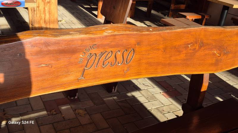 A wooden bench with an engraved inscription in front of the commercial premises on Park and Main Street, Veľké Ludince.