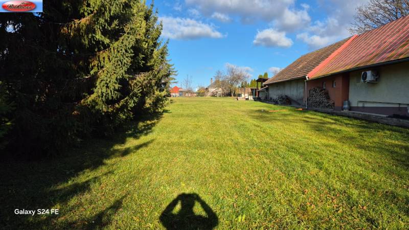 A grassy area with wooden shelters and trees in the park and main road in Veľké Ludince.