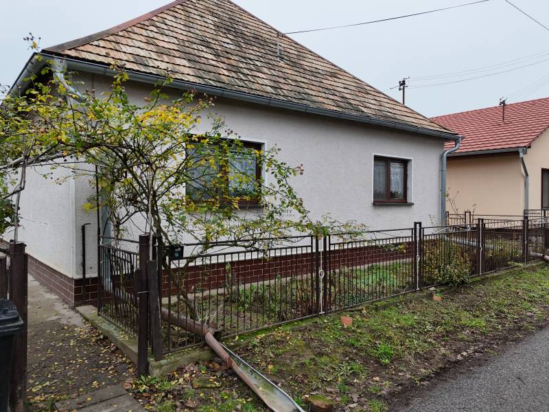 A family house in Hokovce with a ceramic roof and fencing, surrounded by greenery.