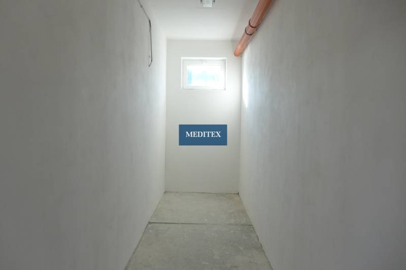 A narrow corridor with a bright window and orange piping, warehouses and halls.