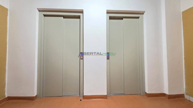 Two closed elevators in a building with white walls and a colorful floor.