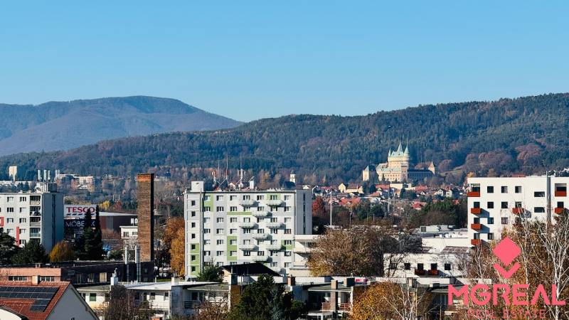 View of Prievidza from I. Krasko Street with nearby buildings and green hills.