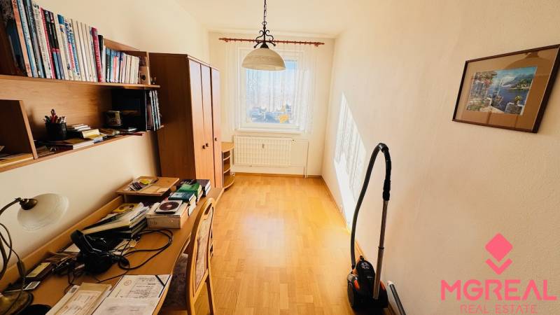 A room in a 4-room apartment with a wooden decor floor, a desk, and shelves.