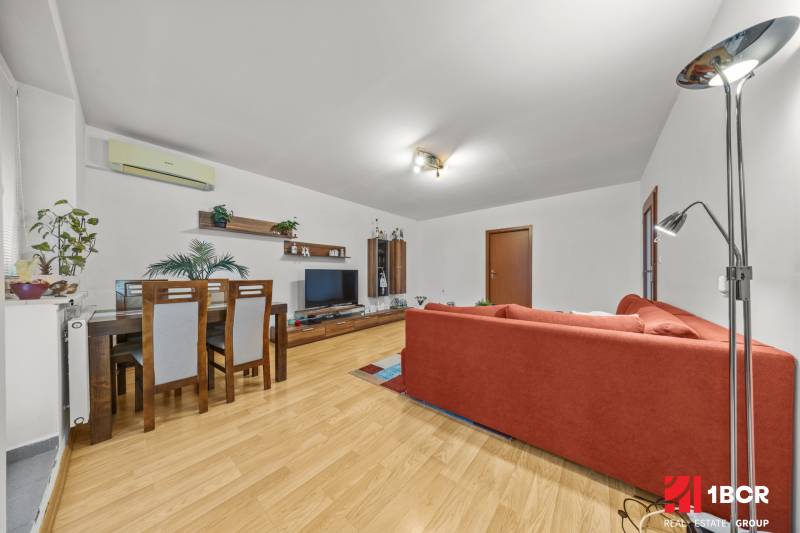 Living room in a two-room apartment with a wooden decor floor and a red sofa.