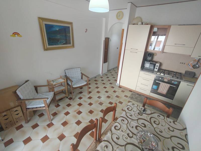 A kitchen in a 2-room apartment with a dining table, chairs, and a painting on the wall.