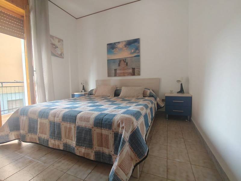 A bedroom in a two-room apartment with a double bed, pictures on the walls, and blue nightstands.