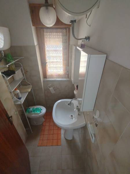 A bathroom in a 2-room apartment with a sink, toilet, and storage shelf.