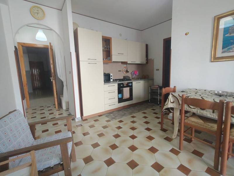 A kitchen of a two-room apartment with a seating area, a kitchen unit, and hexagonal patterned tiles.