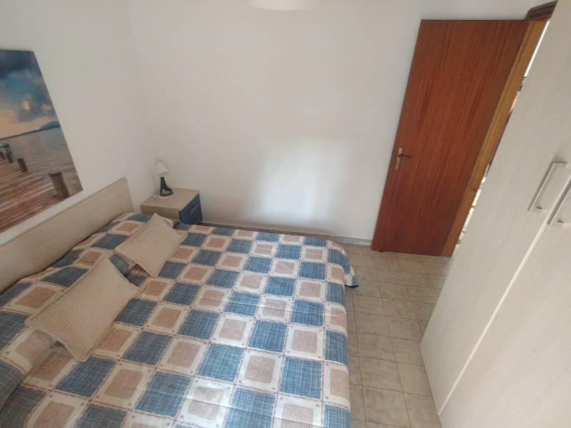 Bedroom in a two-room apartment with a double bed, nightstand, and a picture on the white wall.