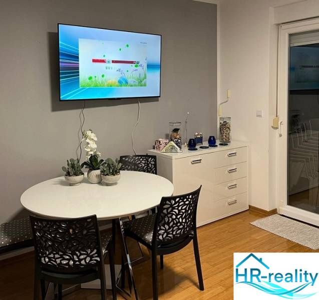 Dining area in a 3-room apartment with a wood-patterned floor and a television.