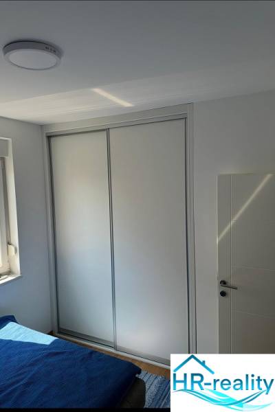 A bedroom in a 3-room apartment with a sliding wardrobe, white walls, and a wooden decor floor.