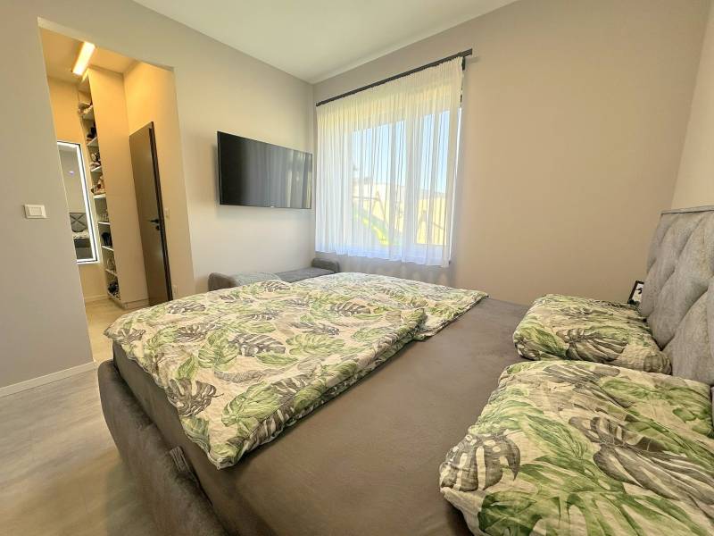 A bedroom in a family house with a wardrobe, a television, and a bed with tropical patterned bedding.