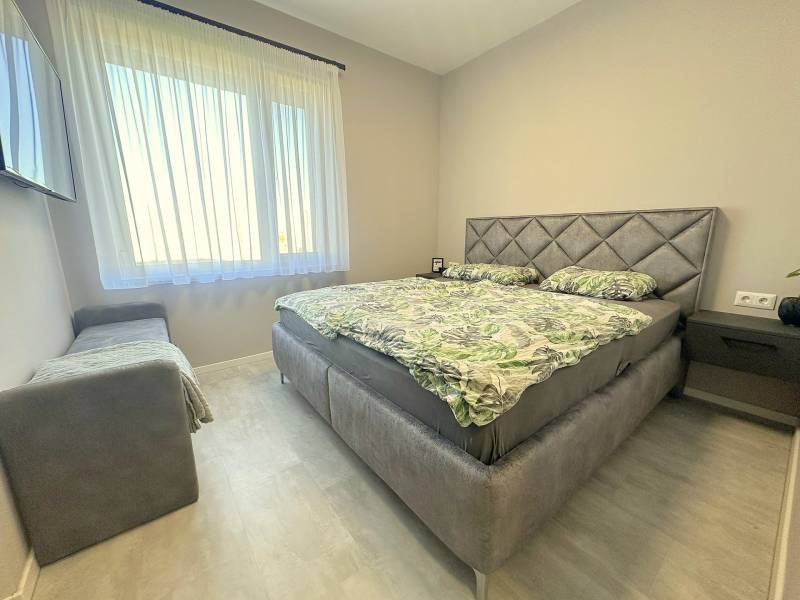 A bedroom in a family house with a bed, sofa, television, and curtains on the window.