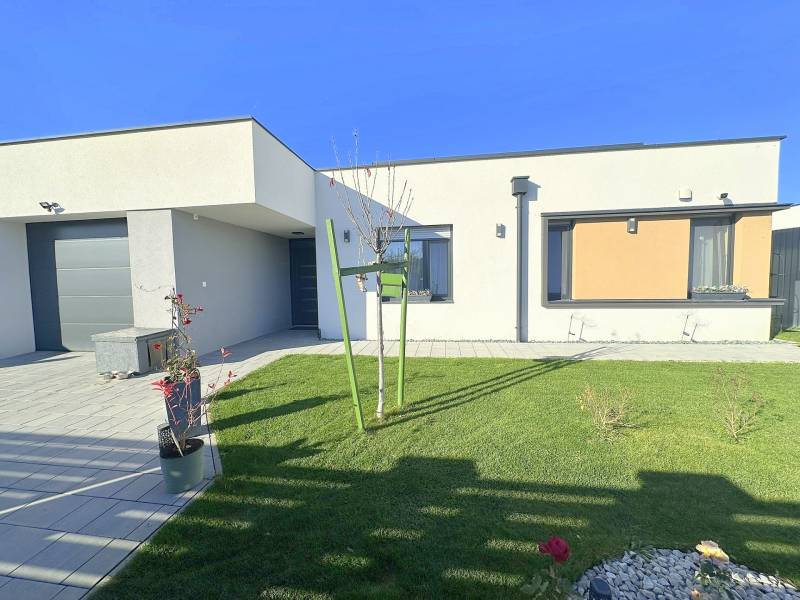 A family house in Mosonmagyaróvár with a green lawn, stone decor, and elegant flowers in pots.