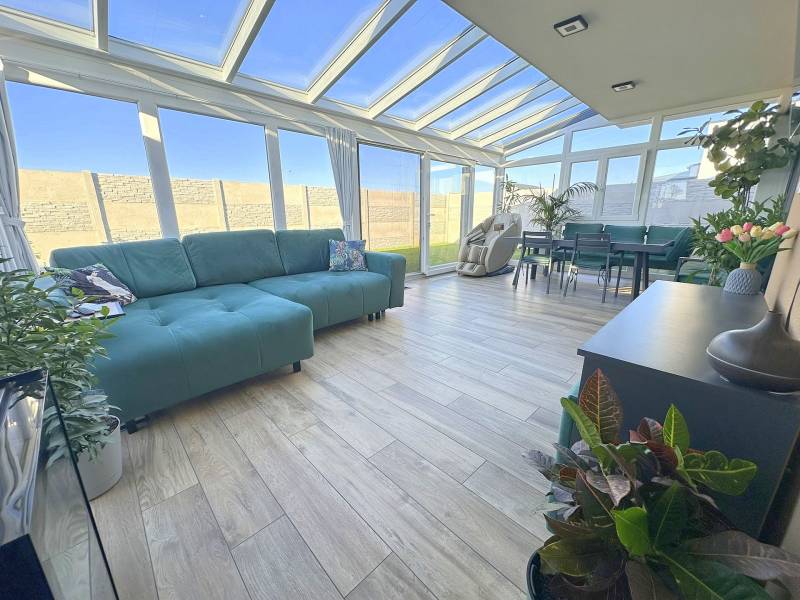 Family house with a glass veranda, sofas, plants, and a wooden decor floor.