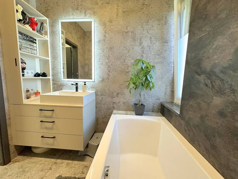 Family house with a bathroom: bathtub, sink, mirror, plant, and storage spaces.
