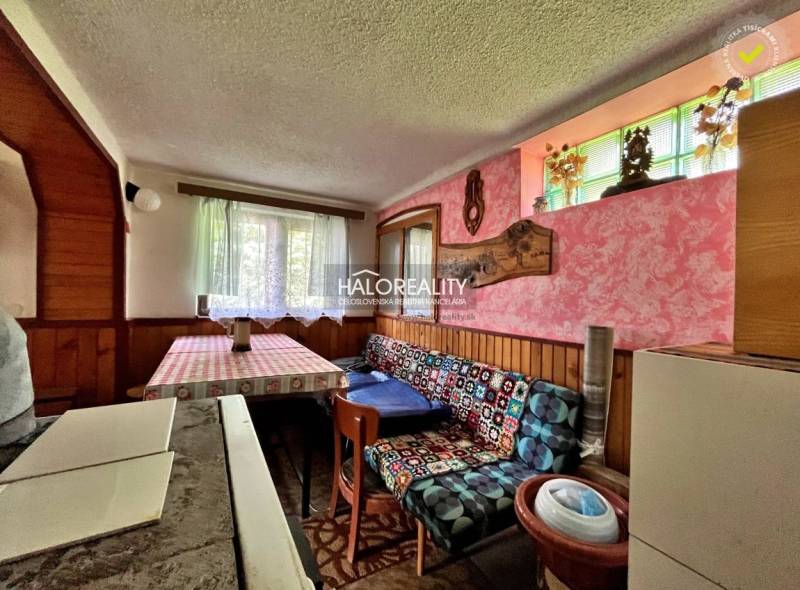 The interior of a cabin with wooden paneling, a colorful sofa, and a striped tablecloth.