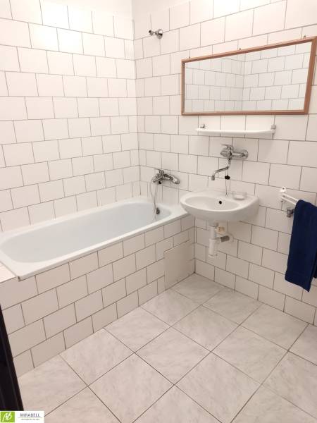 A bathroom in a studio apartment with a bathtub, sink, and white tile cladding.